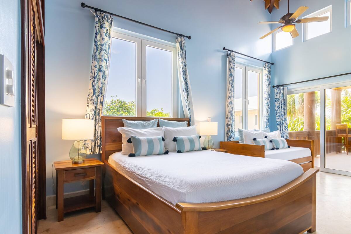 A double bed with a wooden frame and white bedding, two bedside tables with lamps, and a ceiling fan.
