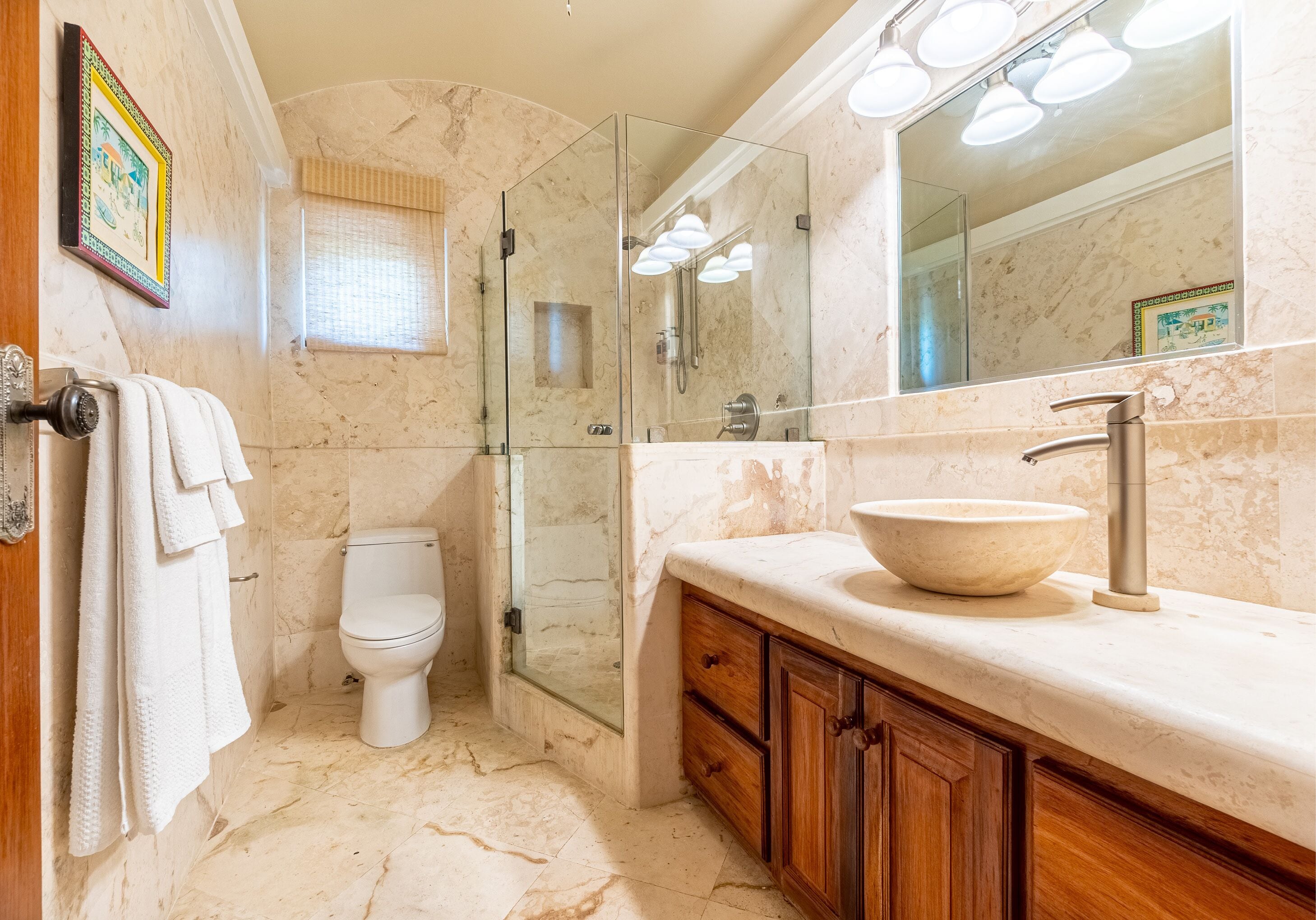 A bathroom with a marble floor, a glass-enclosed shower, a white toilet, wooden cabinets, and a large mirror.
