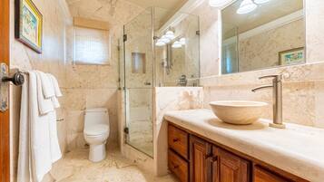 A bathroom with a marble floor, a glass-enclosed shower, a white toilet, wooden cabinets, and a large mirror.