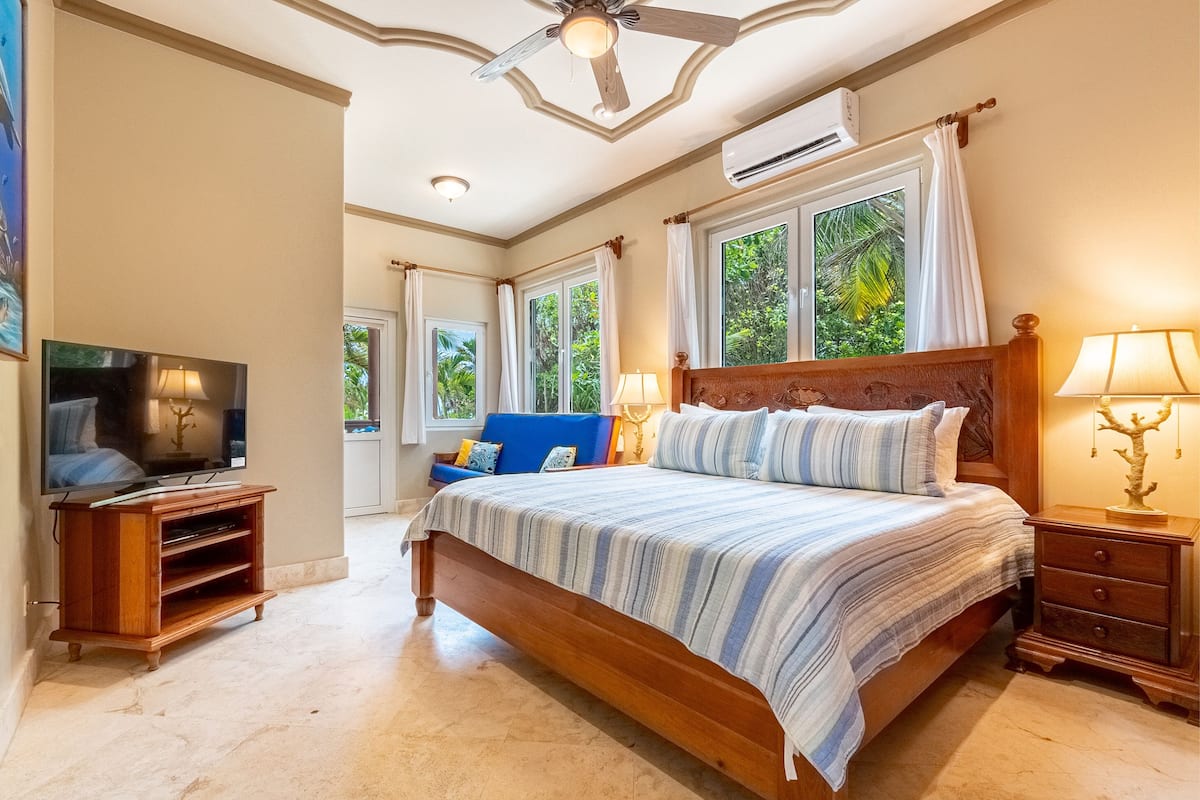 A bedroom with a large bed, a TV, a wooden nightstand, and a ceiling fan.