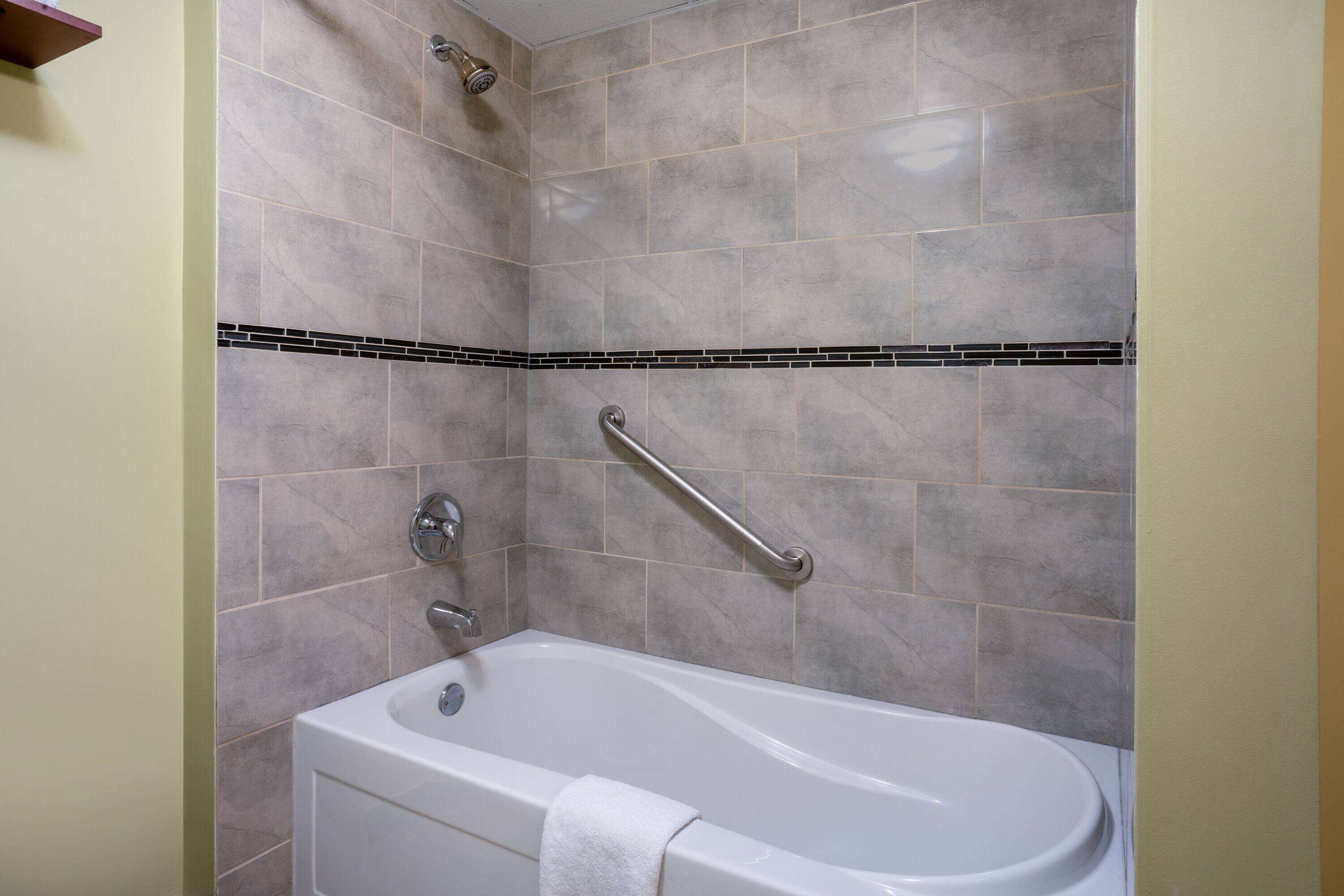 Un baño con bañera, baranda y pared con azulejos.