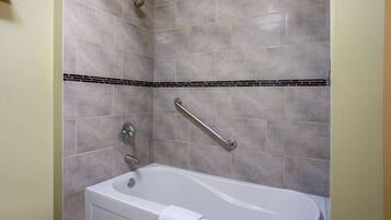 Un baño con bañera, baranda y pared con azulejos.