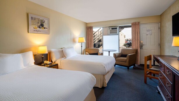 A hotel room with two beds, a desk, a chair, a dresser, and a television.