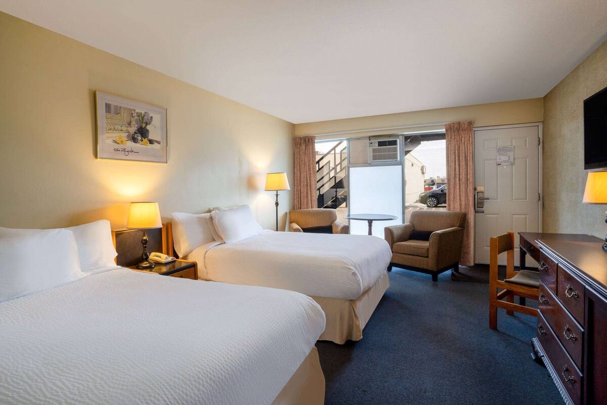 A hotel room with two beds, a desk, a chair, a dresser, and a television.