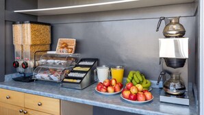 A breakfast buffet with a coffee machine, juice, and fruits.