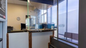 A reception desk with a computer, a clock, and a window with a bench outside.