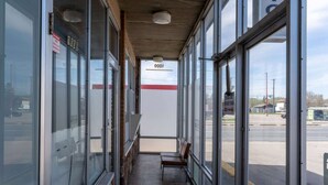 A corridor with glass doors and windows, a bench, and a sign indicating a 24-hour service area.