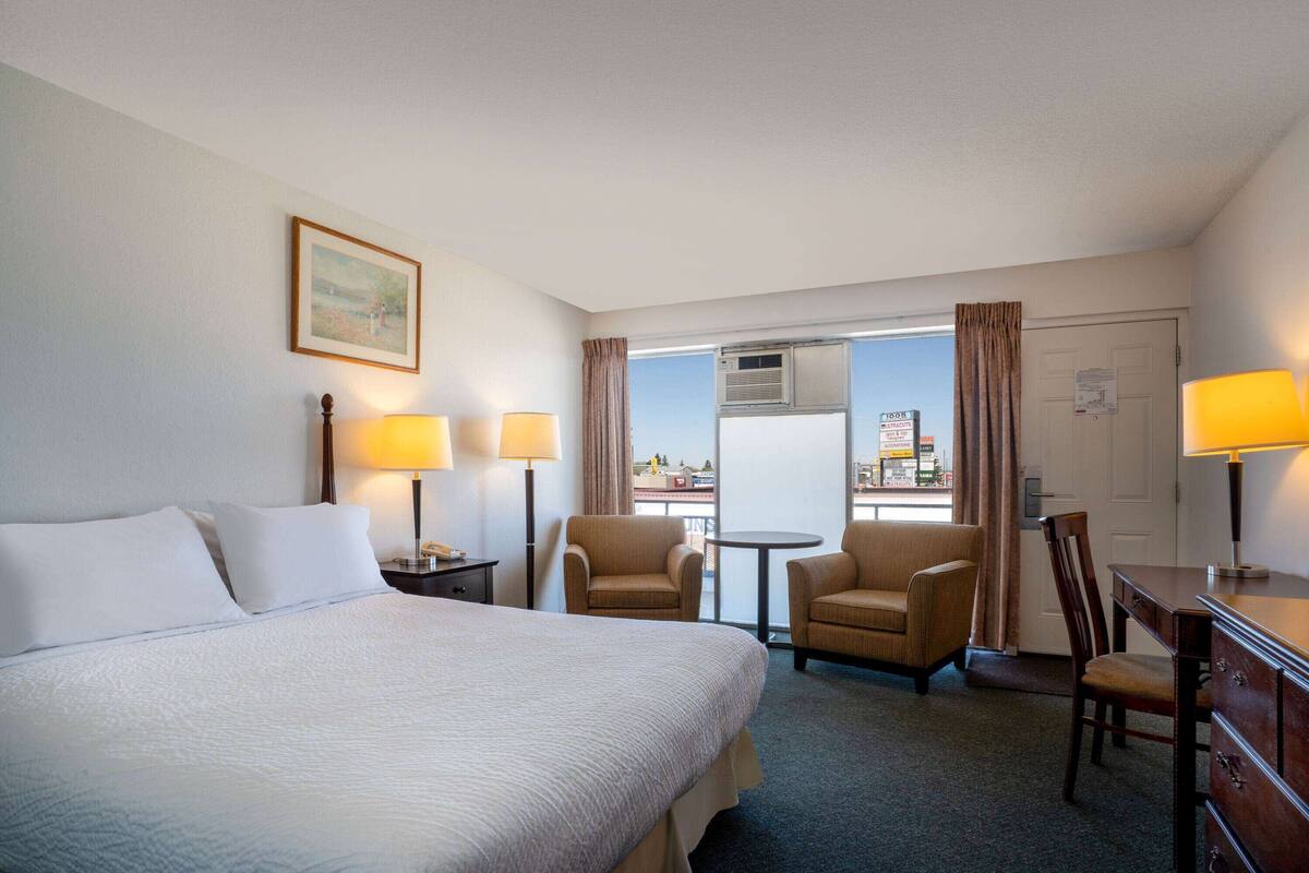A hotel room with a large bed, two armchairs, a small table, and a desk with a lamp.