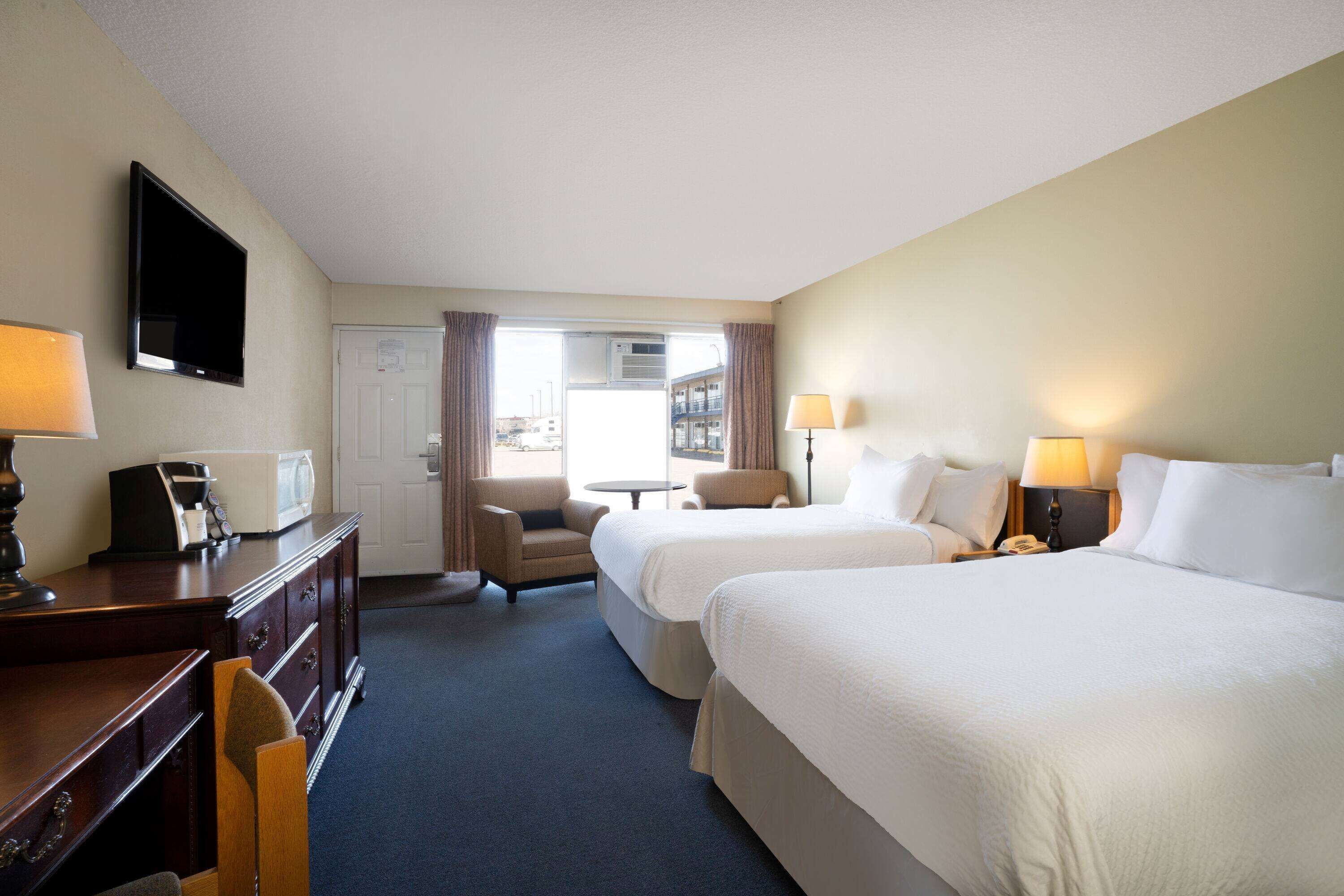 A hotel room with two beds, a desk with a lamp, a chair, a small table, and a TV on the wall.
