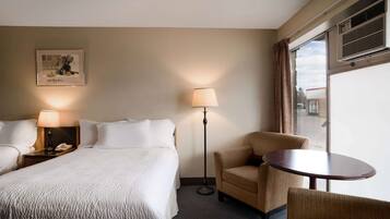 Una habitación de hotel con una cama, dos mesitas de noche, una lámpara, una silla, una mesa y una ventana con cortinas.
