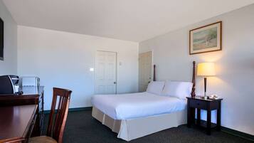 Habitación de hotel con cama, escritorio, silla, lámpara y un cuadro en la pared.