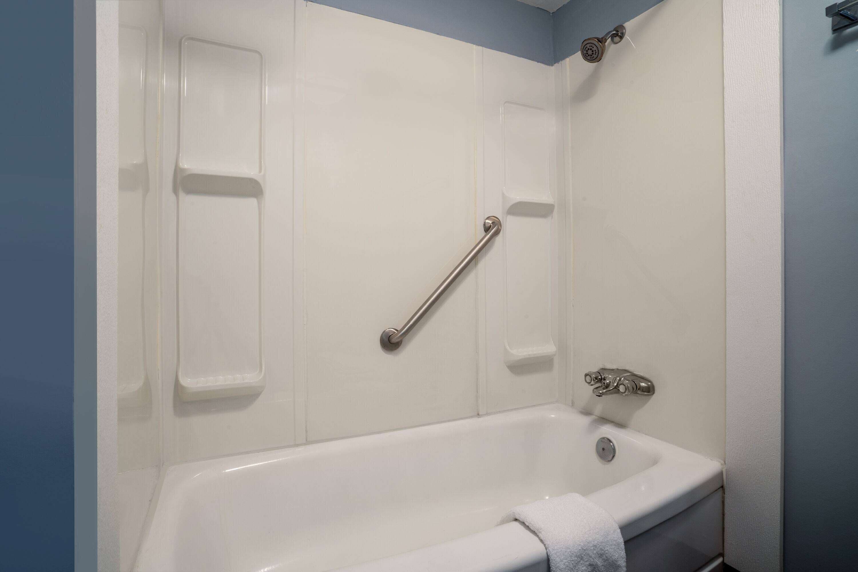 A bathroom with a white bathtub, a grab bar, and a showerhead.