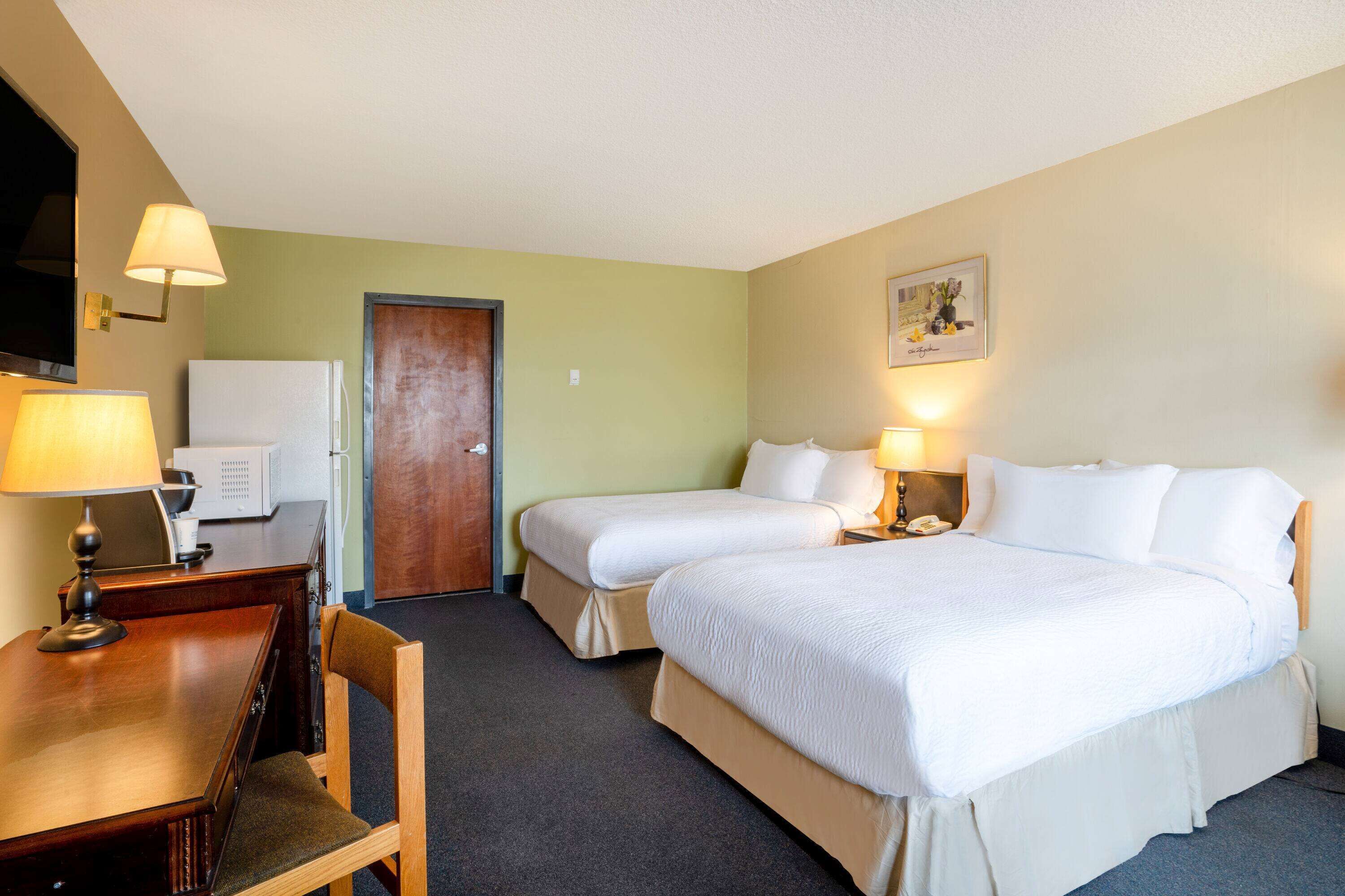 Ein Hotelzimmer mit zwei Betten, einem Schreibtisch mit Stuhl, einem Fernseher und einer Tür.