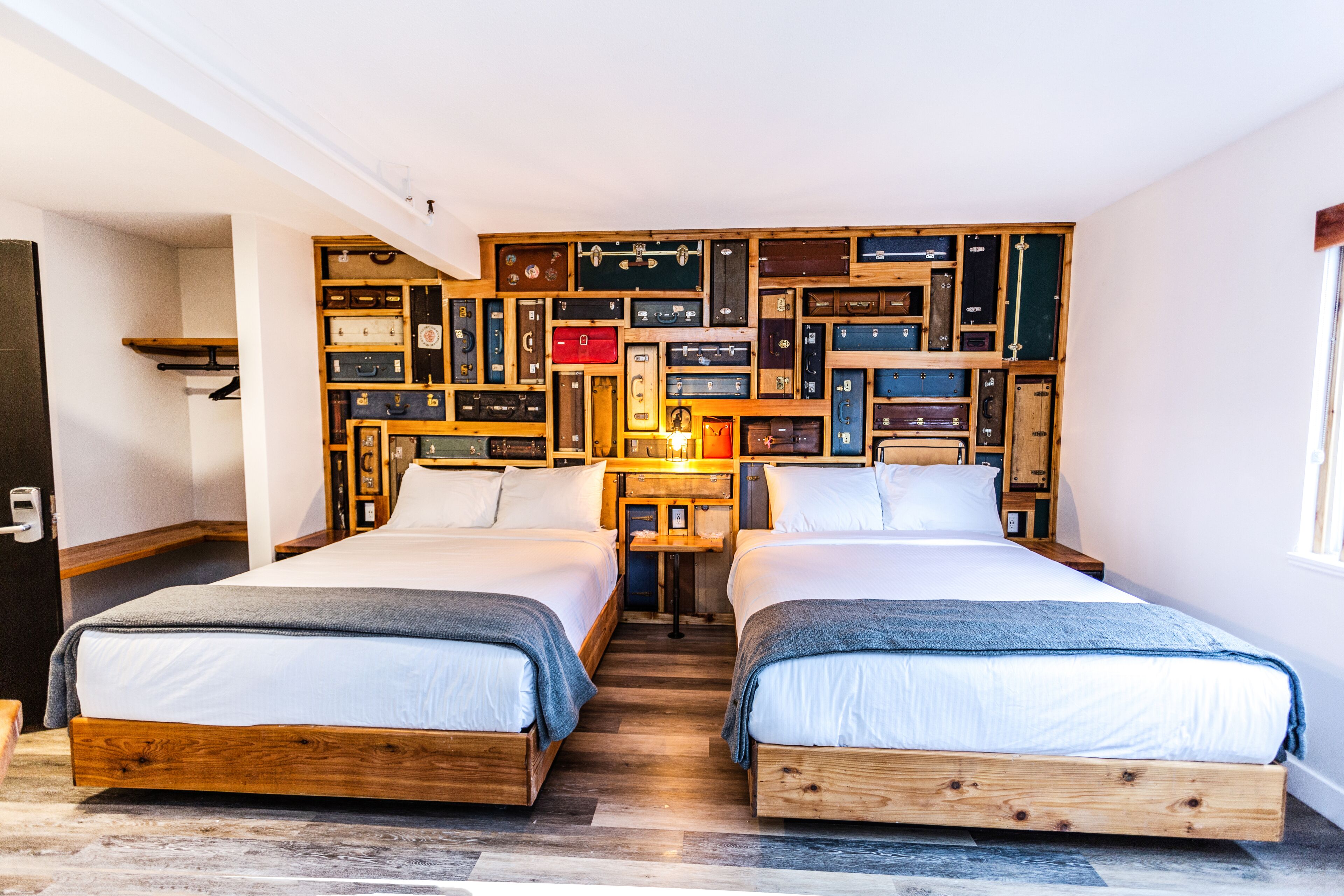 A room with two wooden beds, a wall of suitcases, and a small table with a lamp.