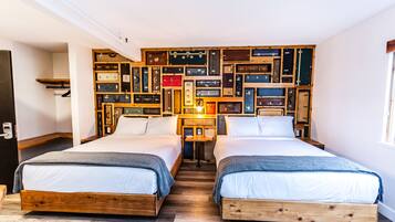 A room with two wooden beds, a wall of suitcases, and a small table with a lamp.
