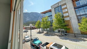 A view of a street with a mountain in the background, a building with multiple signs, and parked vehicles. - Crash Hotel Squamish (Squamish)