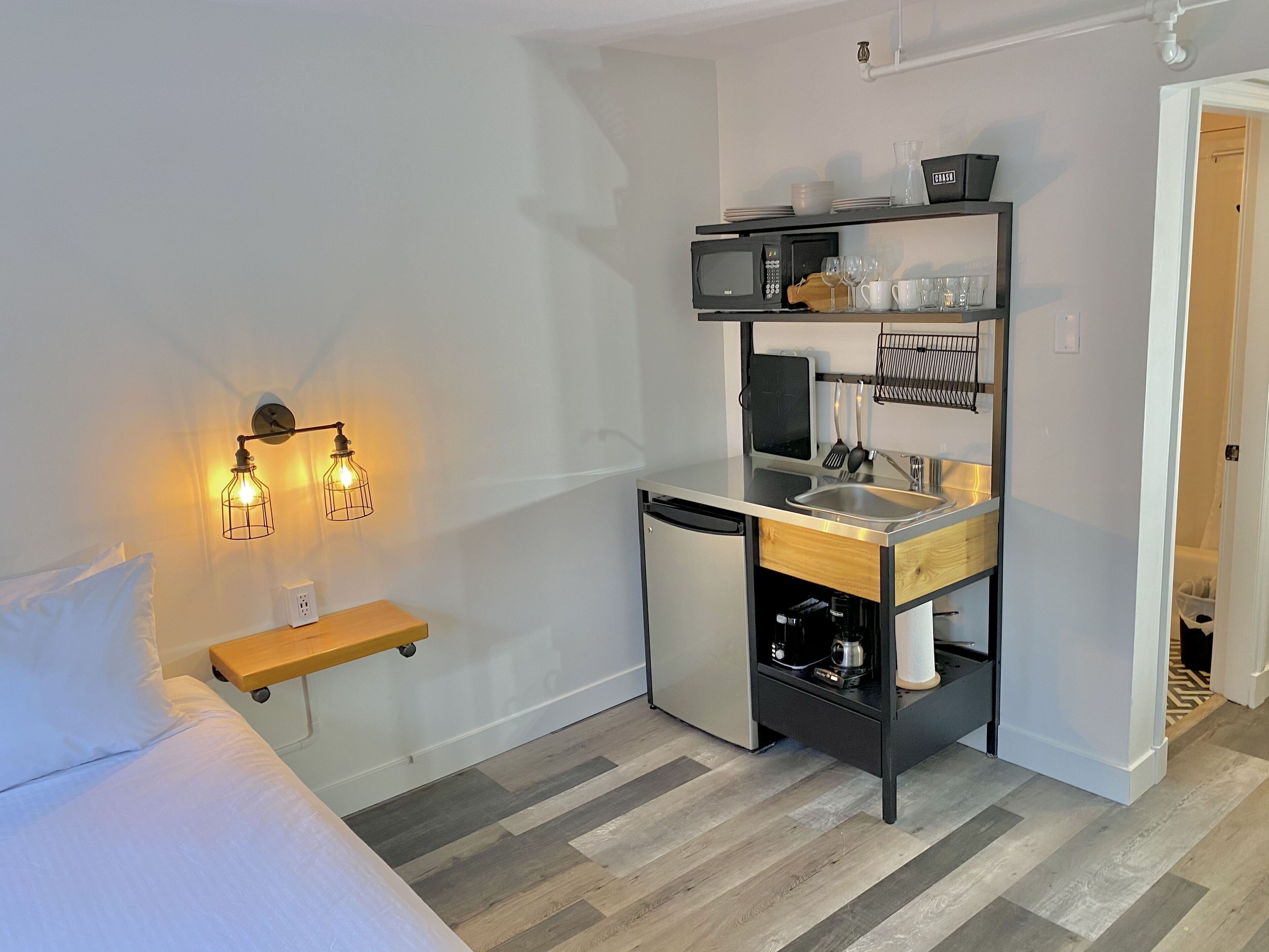 Una kitchenette compacta con un lavamanos, microondas y estanterías.