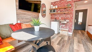 A compact living space with a dining table, a sofa, a small kitchen area with a microwave and a sink, and a door leading to another room. - Crash Hotel Squamish (Squamish)