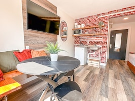 A compact living space with a dining table, a sofa, a small kitchen area with a microwave and a sink, and a door leading to another room.