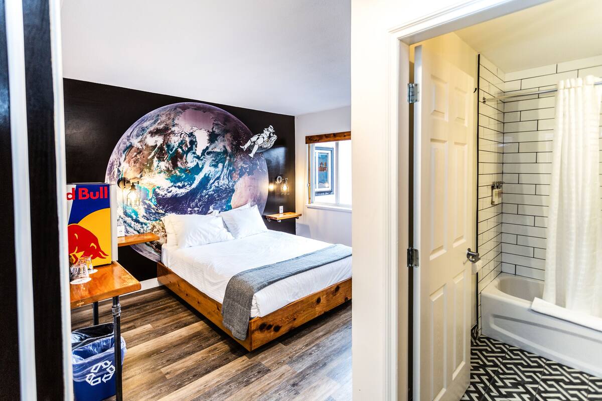 A bedroom with a bed, a Red Bull poster, a globe mural, and a bathroom with a shower and tiled floor.