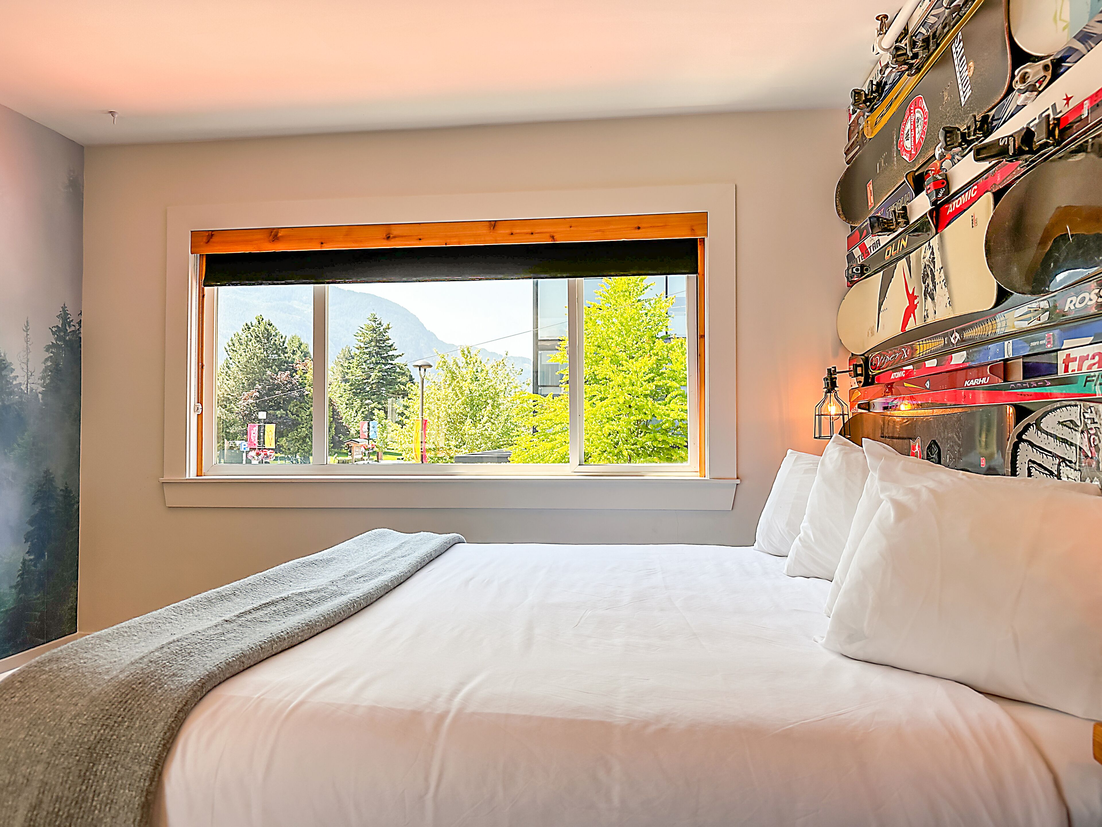 A bedroom with a large bed, a window with a view of trees and mountains, and a wall with various items.