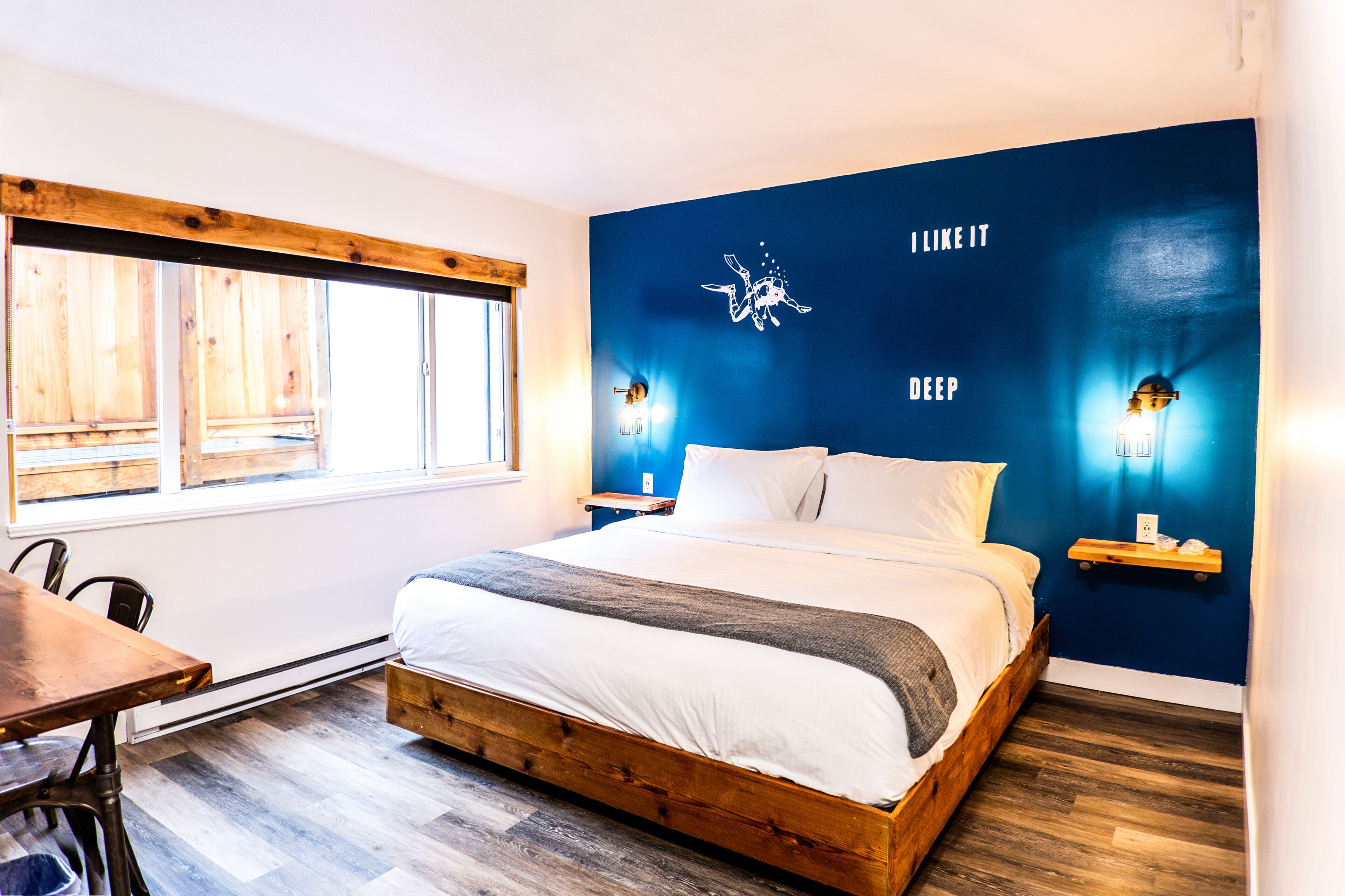 Une chambre avec un lit en bois, une fenêtre et un mur orné d’une fresque bleue.