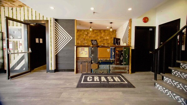 A hotel lobby with a modern design, featuring a geometric patterned wall, a reception desk, and a staircase with a patterned railing.