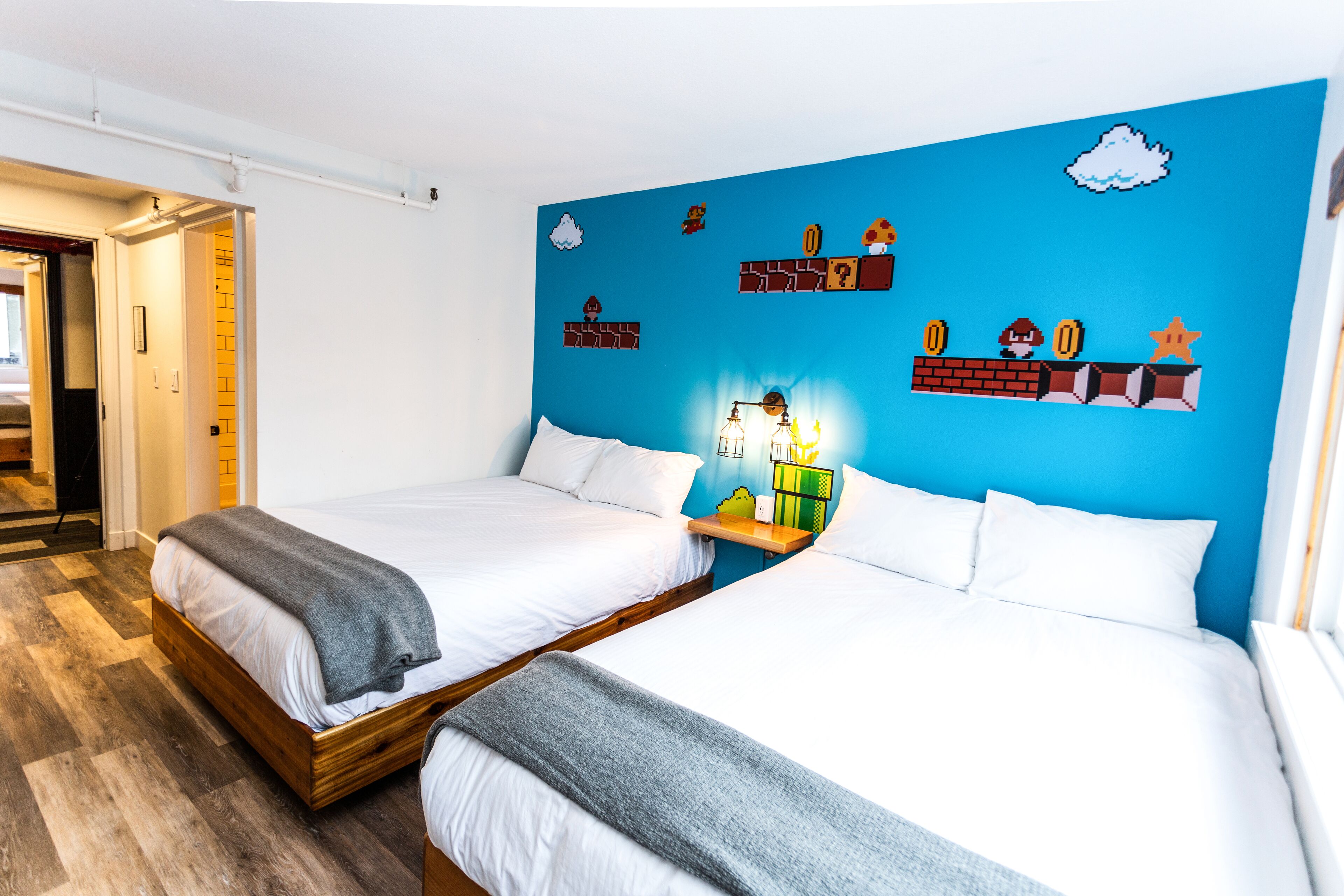 A hotel room with two beds, a blue accent wall, and a small shelf with decorative items.