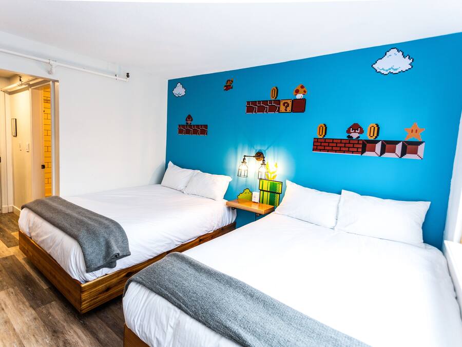 A hotel room with two beds, a blue accent wall, and a small shelf with decorative items.