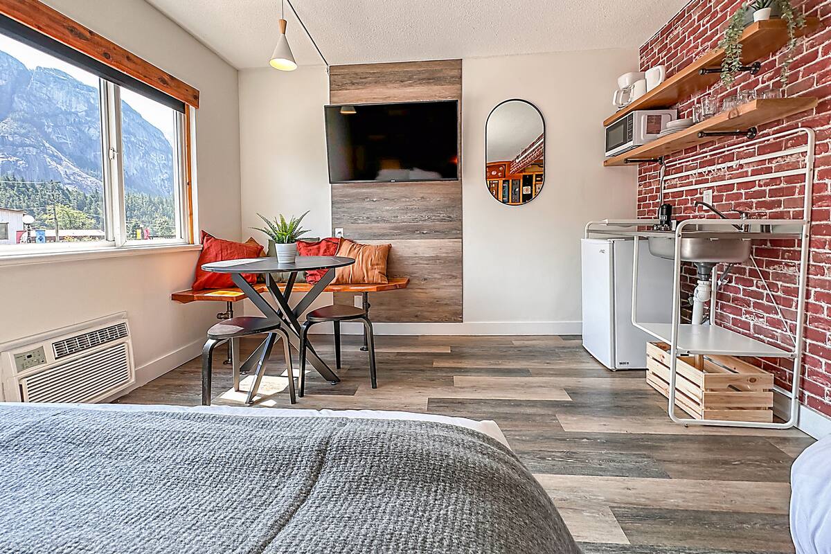 A modern kitchen with a brick wall, wooden shelves, and a dining area with a table and chairs.