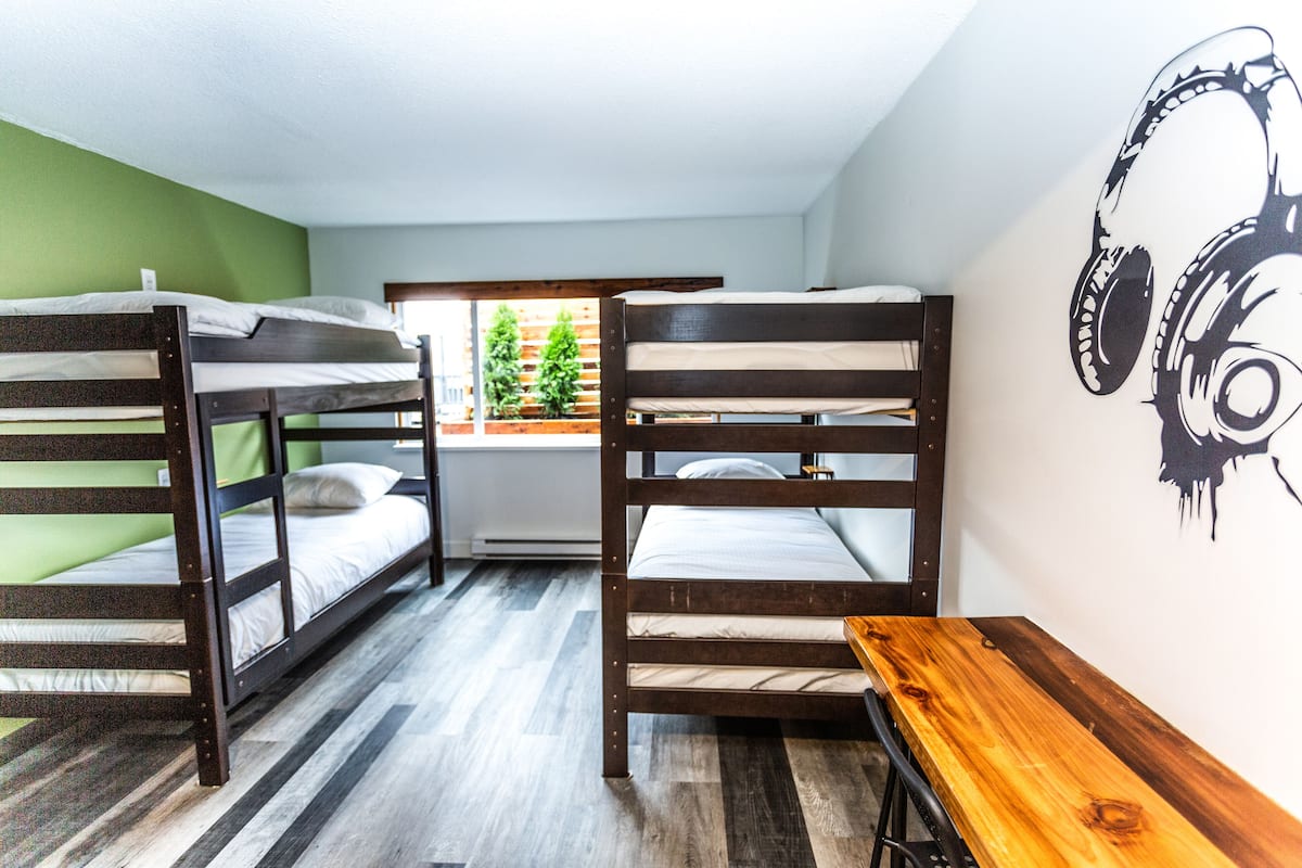 A dormitory room with bunk beds, a wooden bench, and a wall mural.