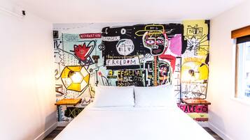A bedroom with a bed centered in the room, a wall mural with various words and symbols, and a window on the right side.