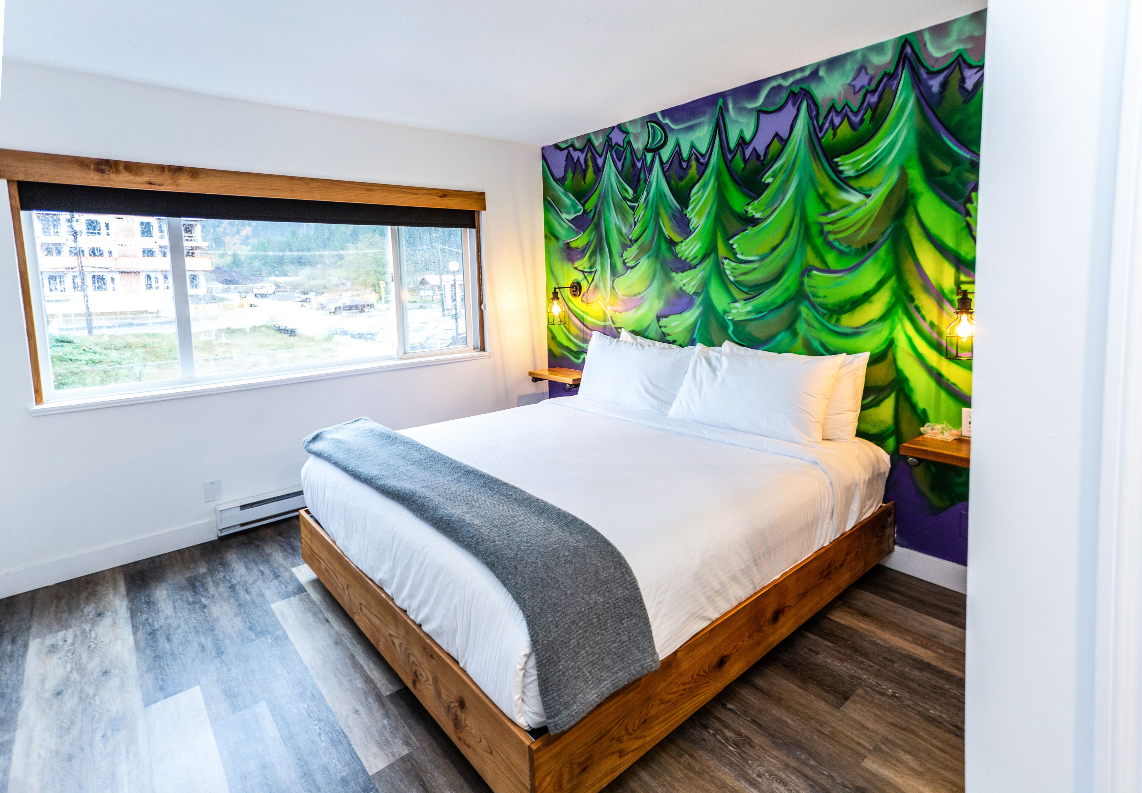 A bedroom with a bed, a window, a wall mural, and a nightstand.