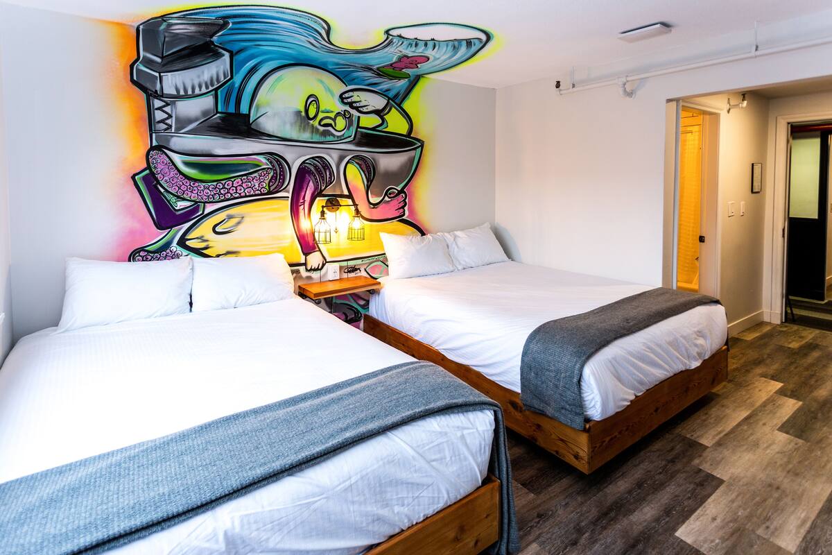 A hotel room with two beds, a colorful mural on the wall, and a wooden floor.