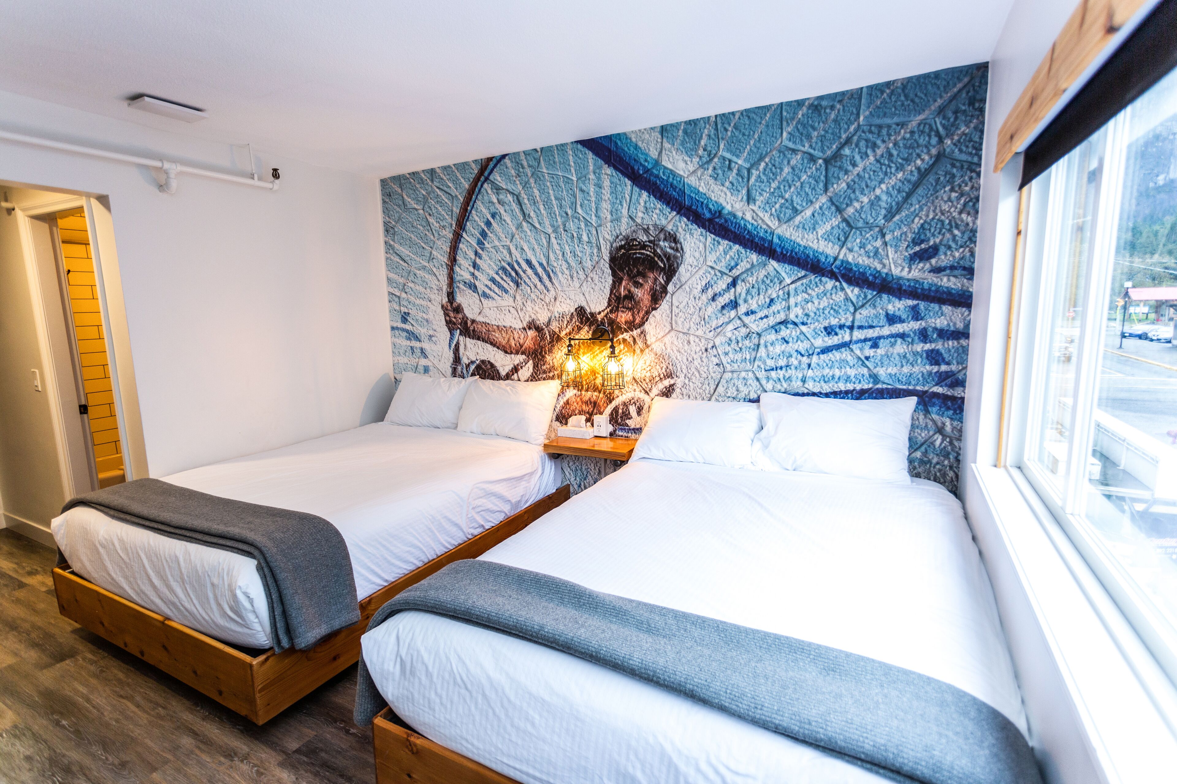 Habitación de hotel con dos camas, un mural grande en la pared y una ventana con vistas.