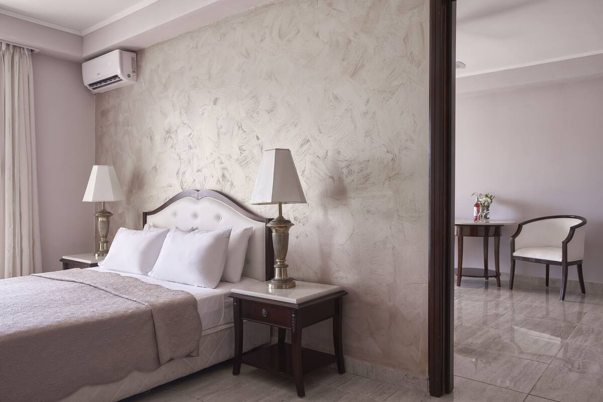 Une chambre d’hôtel avec un lit, des lampes de chevet, une table de chevet, une chaise et une petite table sur laquelle est posé un vase.