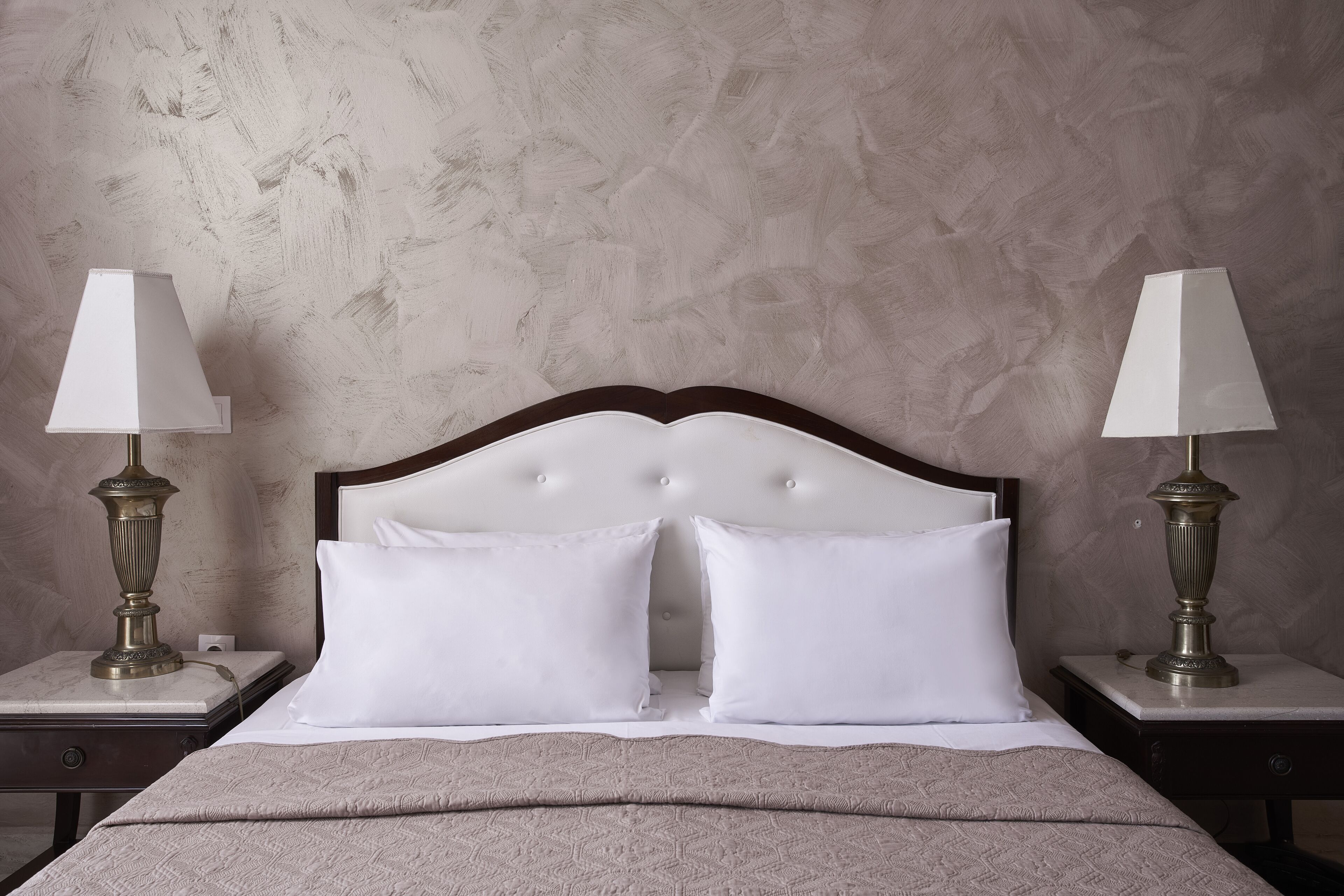 A neatly made bed with white linens, two bedside tables with lamps, and a textured wall behind.