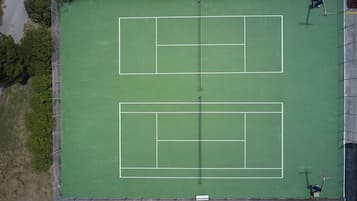 A tennis court with a net, surrounded by a fence, and trees in the background.