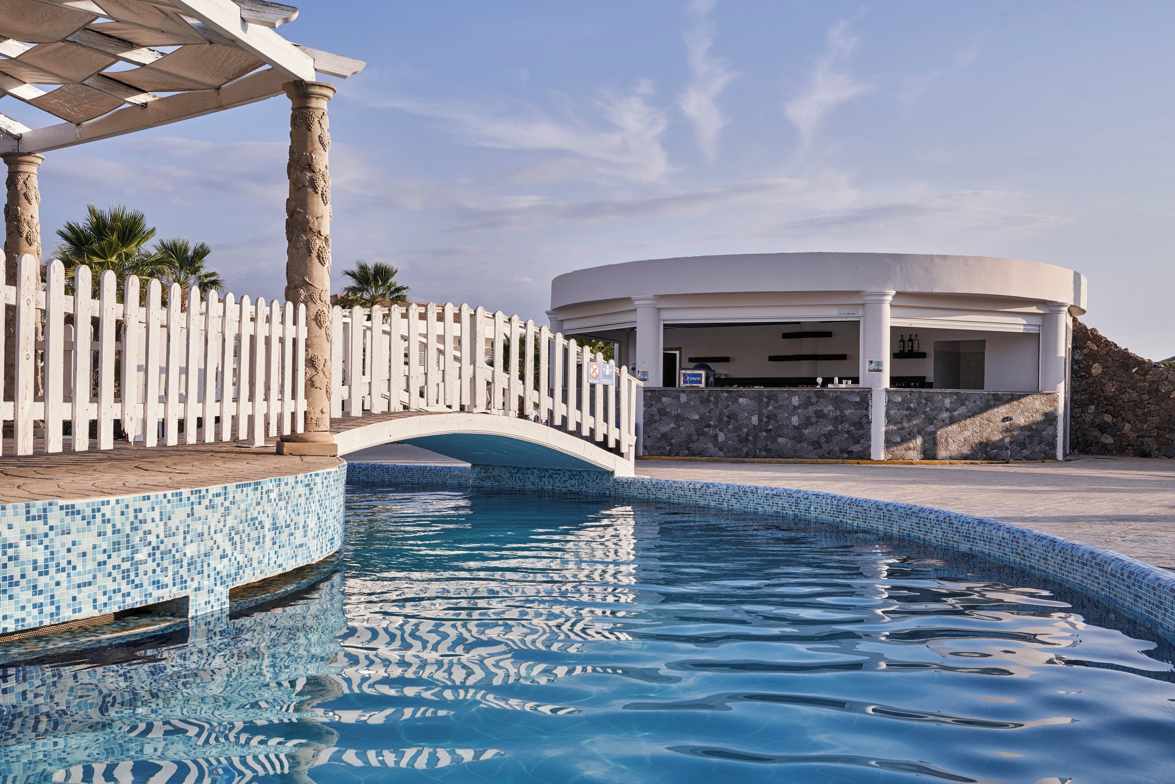 A pool area with a white fence, a bridge, and a building with a stone facade.