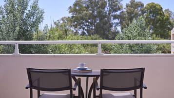 A balcony with two chairs and a table, a white railing, and a view of trees and greenery.