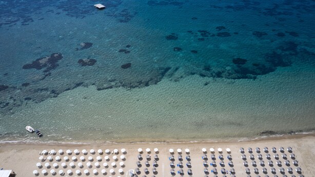 Vista aérea de una playa con hileras de sombrillas y un bote cerca de la orilla.