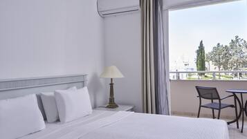 A hotel room with a bed, a nightstand with a lamp, a chair, and a view of the outdoors.