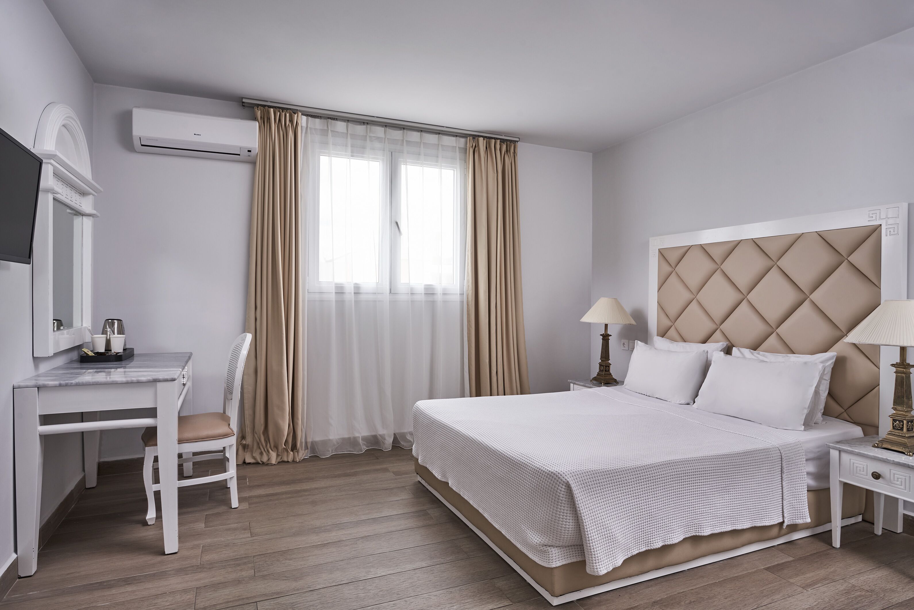 A hotel room with a bed, a desk, a chair, a lamp, and a window with curtains.
