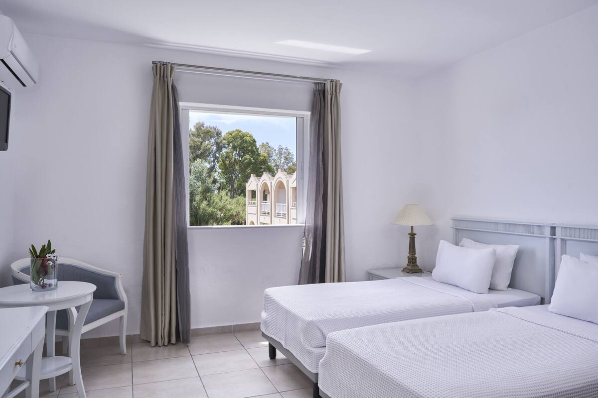 Une chambre d’hôtel avec deux lits, un bureau, une chaise et une fenêtre avec des rideaux.