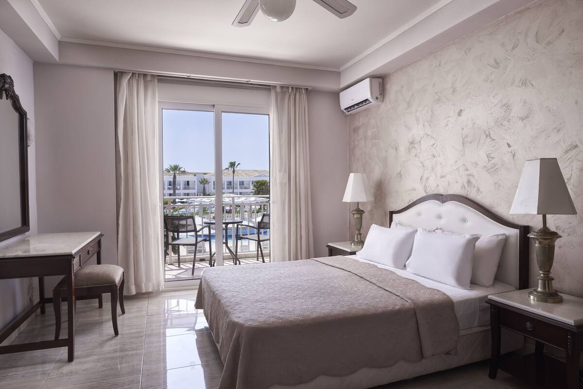 Une chambre d’hôtel équipée d’un lit, d’un bureau, d’une chaise et offrant une vue sur une piscine et des bâtiments.