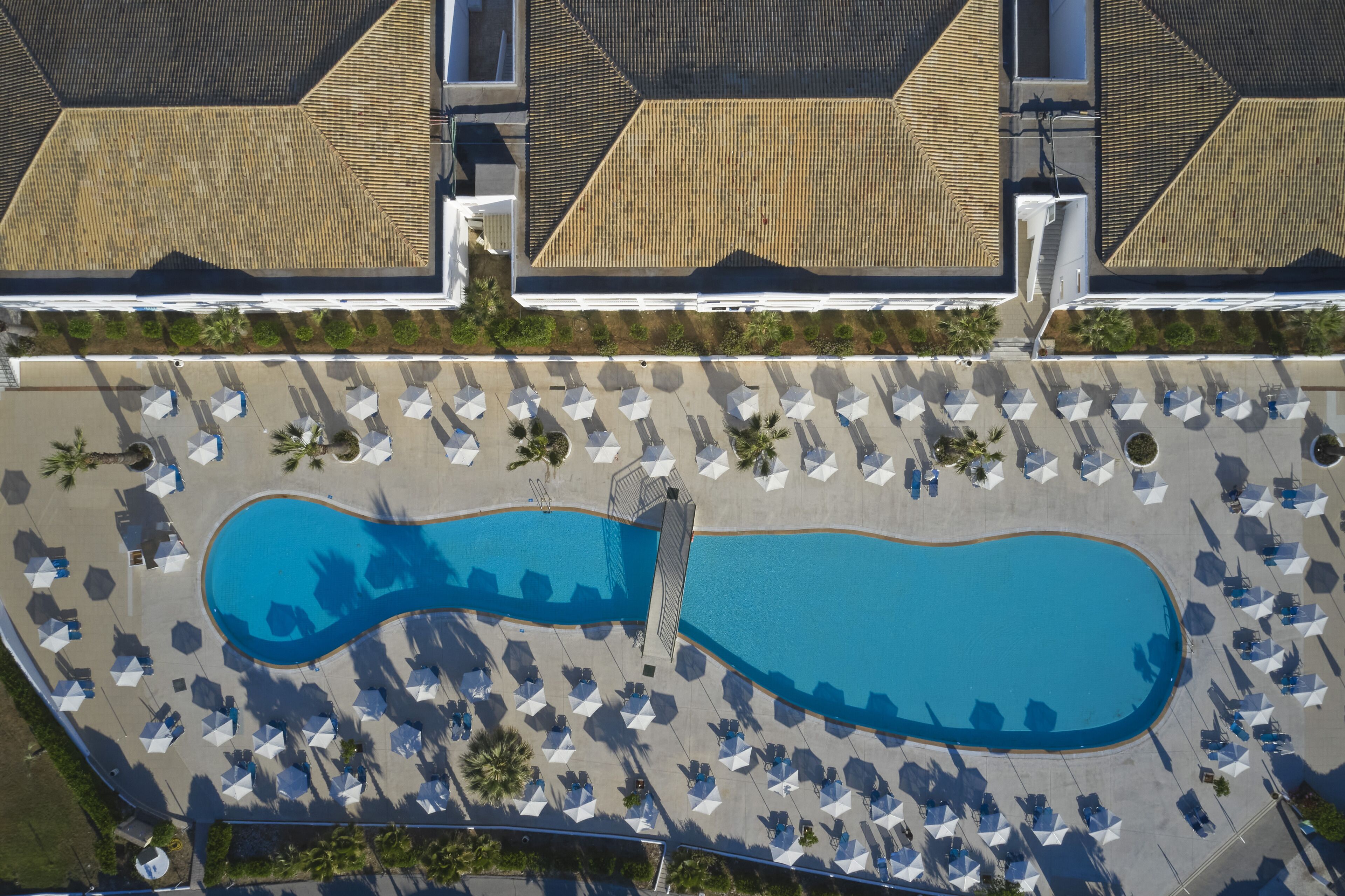 Luchtbeeld van een resort met een groot zwembad, ligbedden en een overdekt gebied met parasols.
