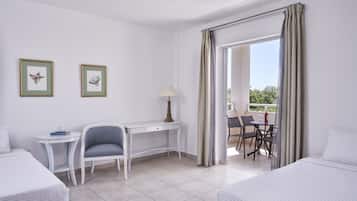 A hotel room with two beds, a desk, a chair, a small table with a lamp, and a balcony with a table and chairs.