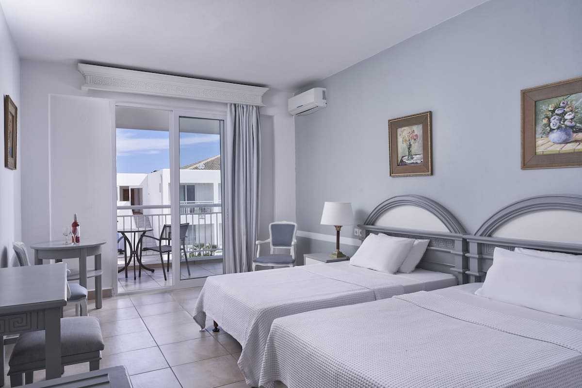 Une chambre d’hôtel avec deux lits, un balcon, un coin repas et une vue sur l’extérieur.