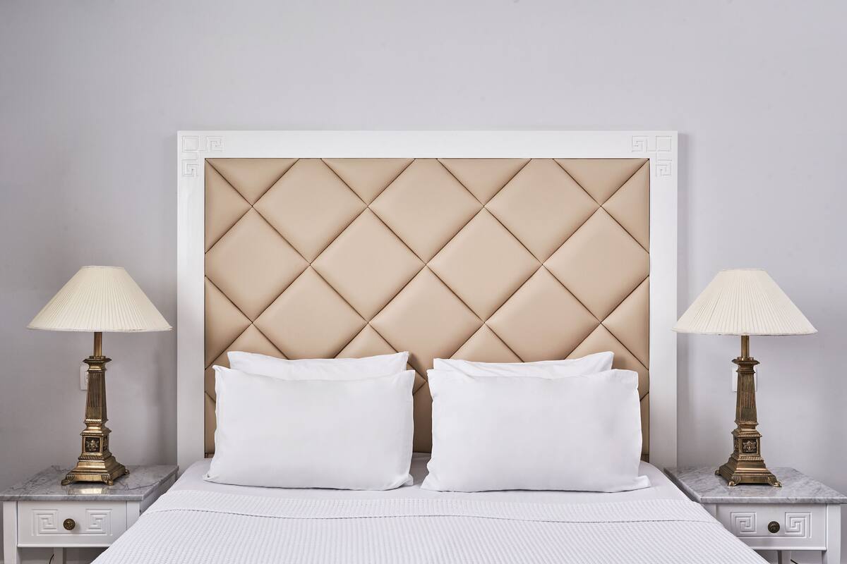 Un lit avec une tête de lit capitonnée, deux tables de chevet avec des lampes et un couvre-lit blanc.