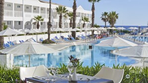 Zona de comedor junto a la piscina con una mesa preparada para dos, con vistas a una piscina con sombrillas y sillas de descanso.